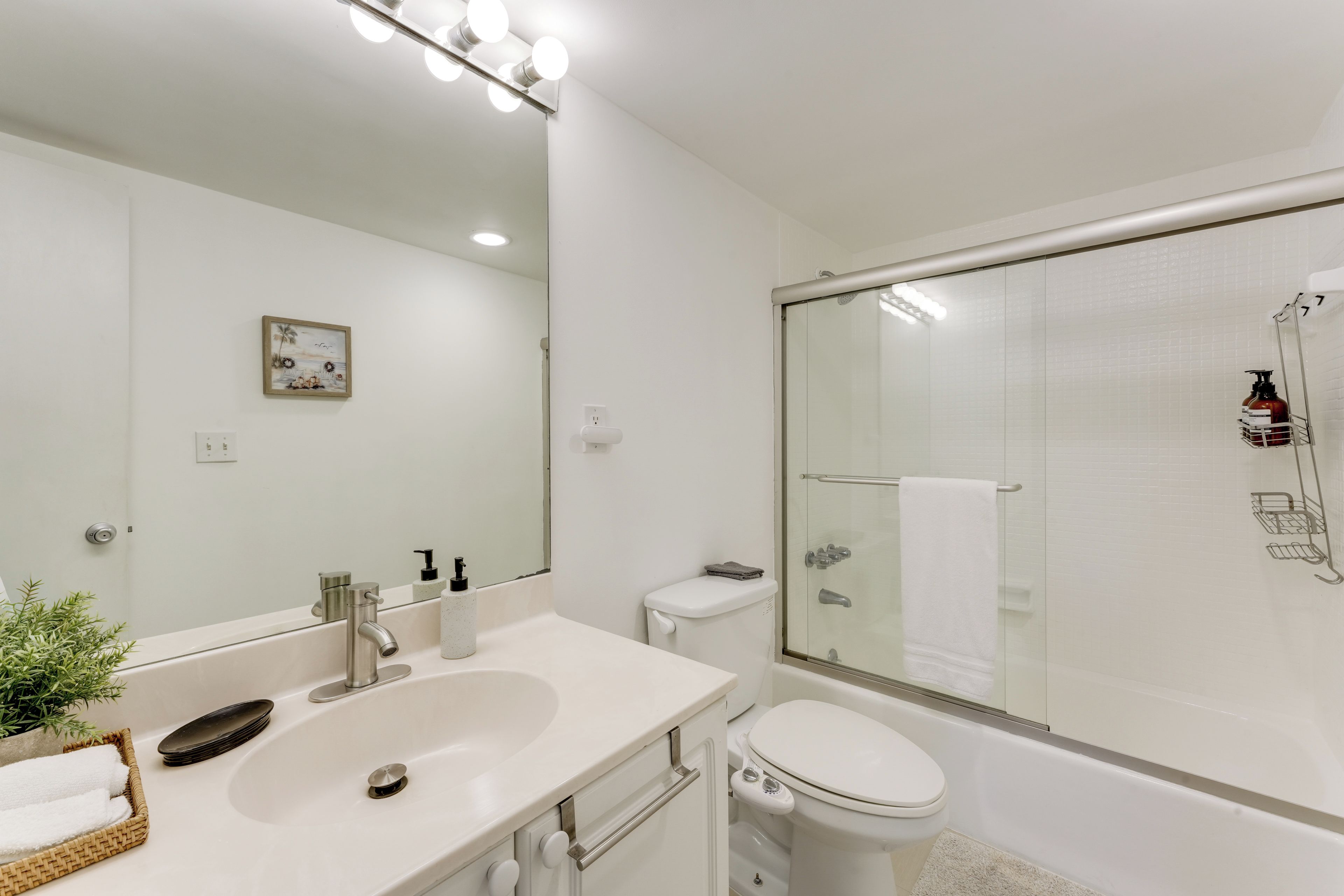 A modern bathroom with a large mirror, a sink, a toilet, and a glass-enclosed shower.