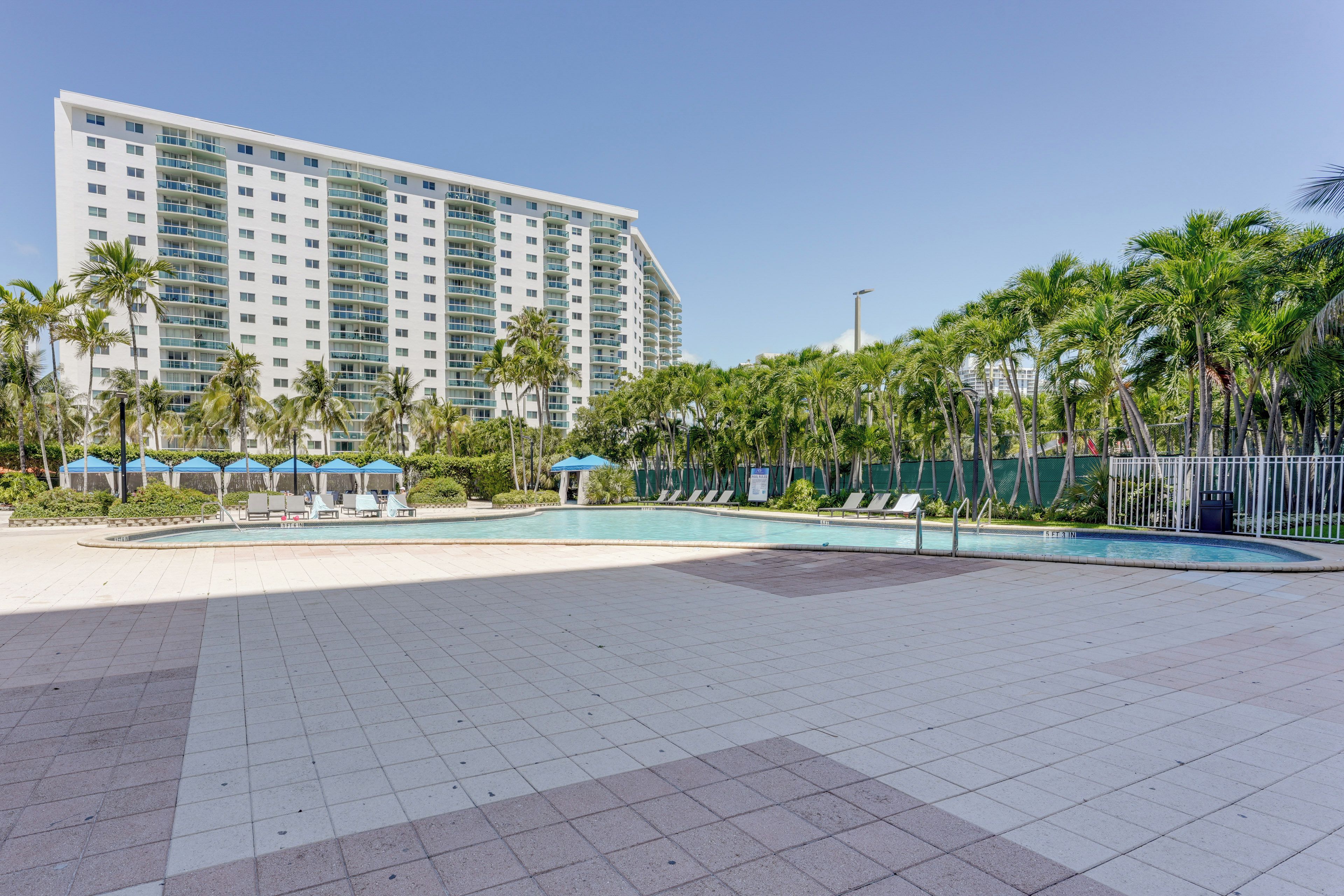 Un hotel con un amplio área de piscina, palmeras y un edificio alto al fondo.