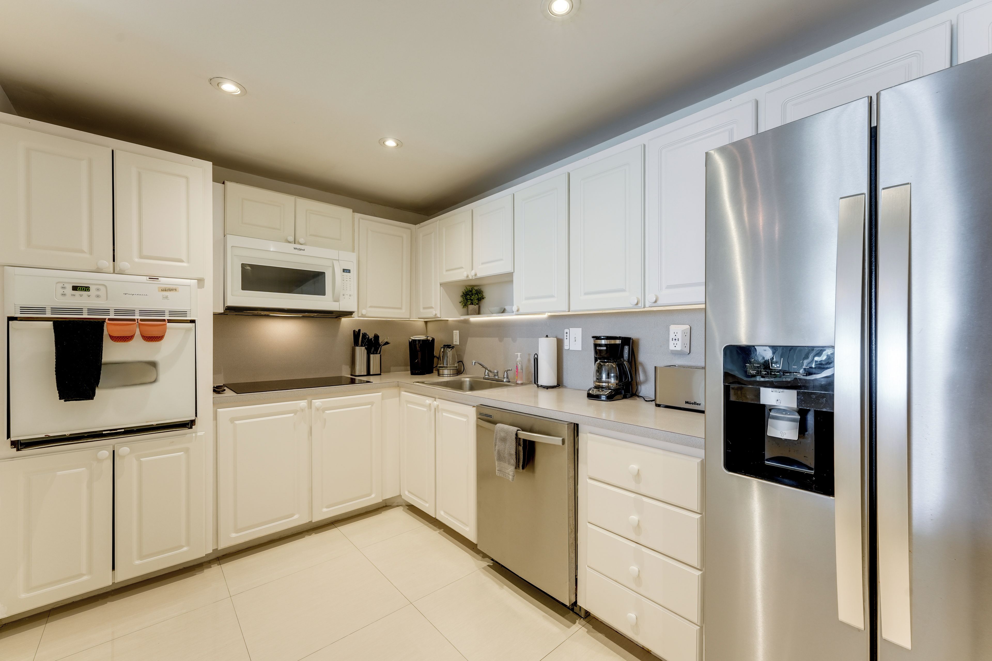 A modern kitchen with white cabinetry, stainless steel appliances, and a built-in dishwasher.