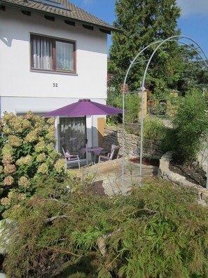 Ein Haus mit einer Terrasse, einer Hausnummer 32 und einem violetten Sonnenschirm.