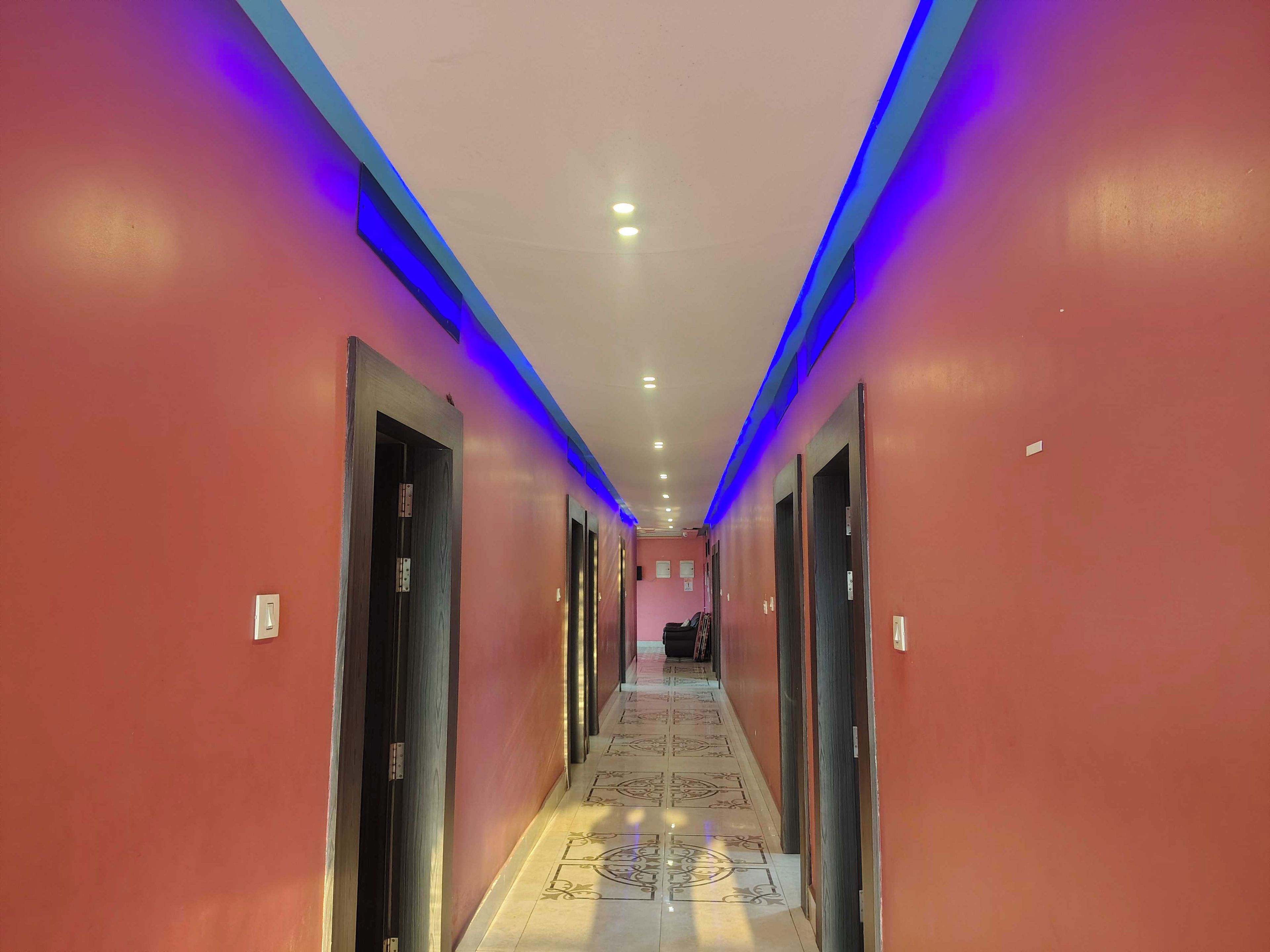 A hotel corridor with doors on both sides, a patterned floor, and blue lighting along the ceiling.