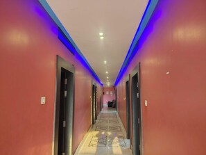 A hotel corridor with doors on both sides, a patterned floor, and blue lighting along the ceiling.