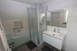 Ein modernes Badezimmer mit einer gläsernen Dusche, einem weißen Waschbecken und einem Spiegel darüber.