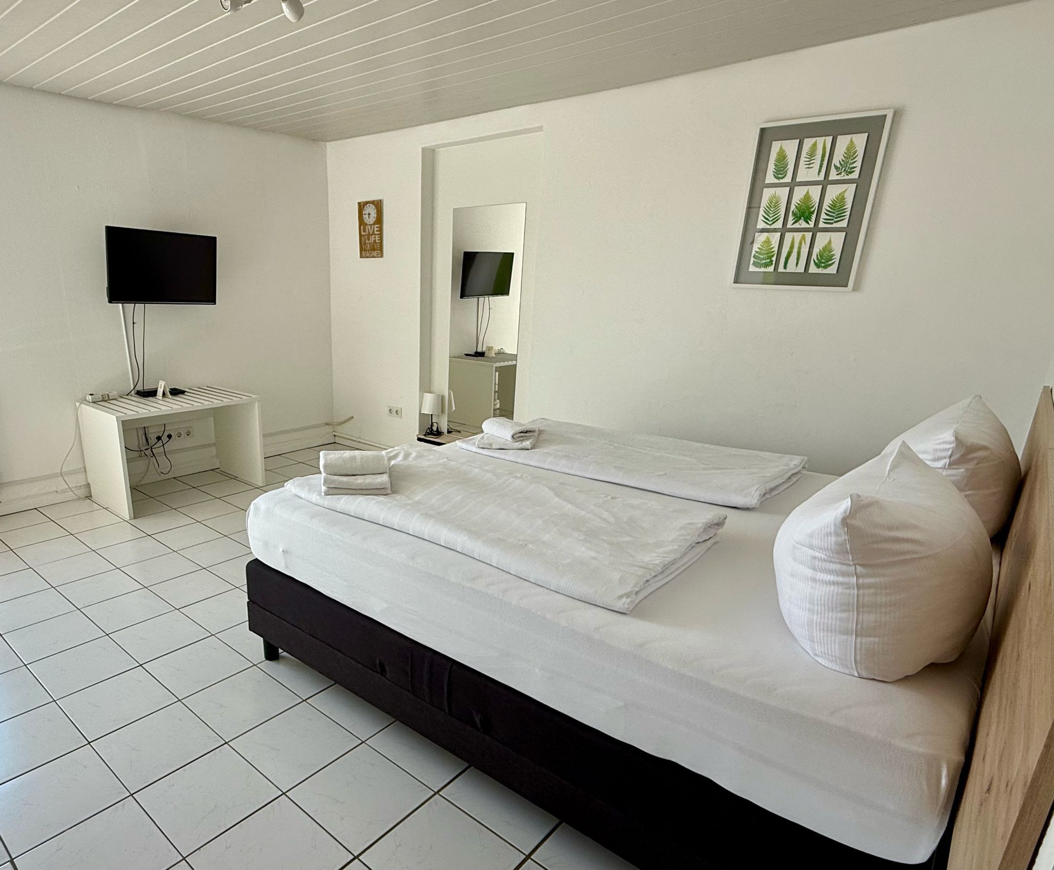 Un dormitorio con cama, mesita de noche, televisión y espejo.