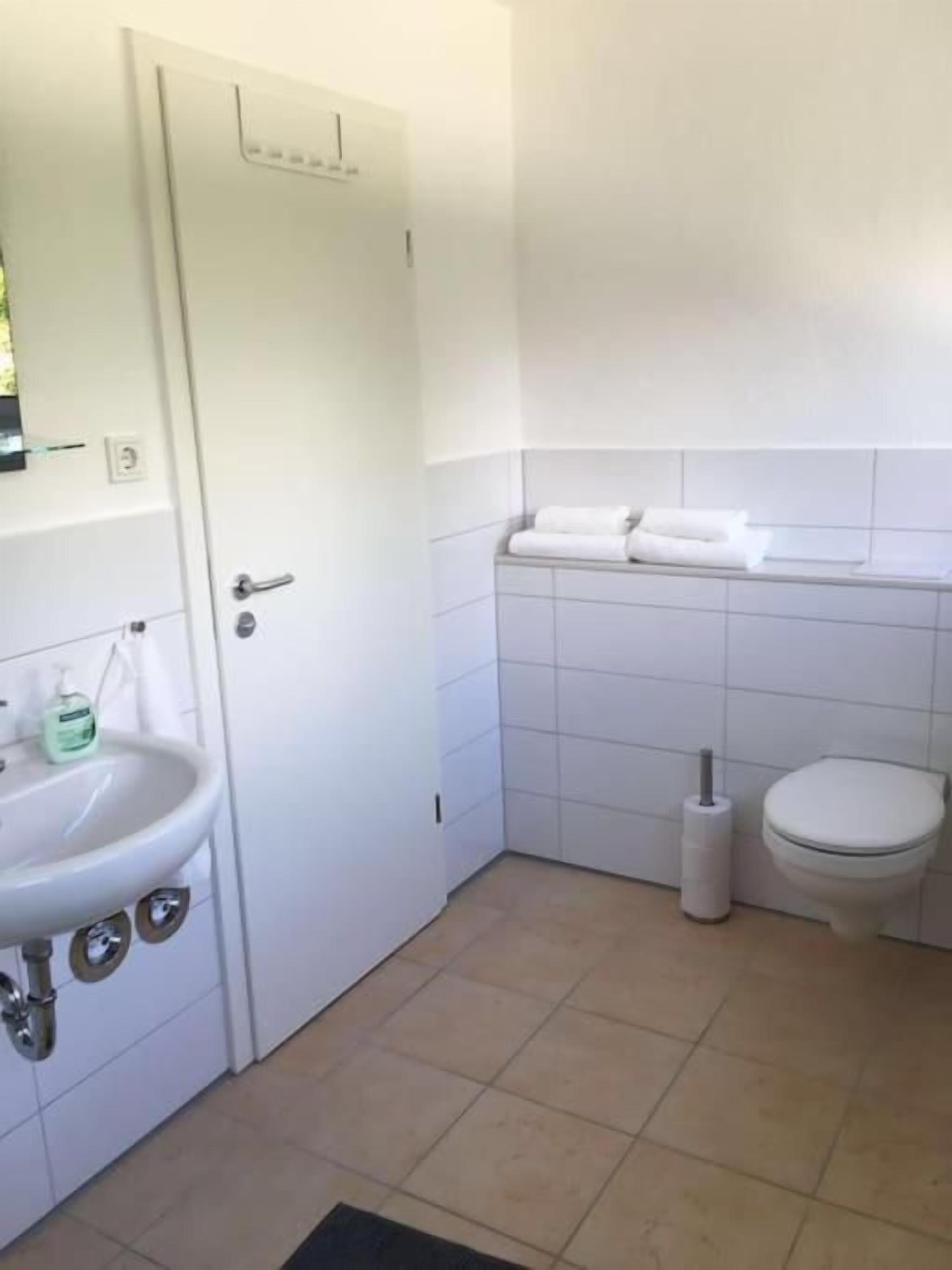 A bathroom with a white sink, toilet, and a small trash bin.