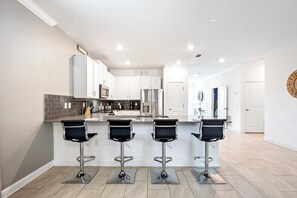 A modern kitchen with white cabinets, stainless steel appliances, and a central island with four bar stools. - Lakeview Villa w/ Themed Rooms & Pool (Kissimmee)