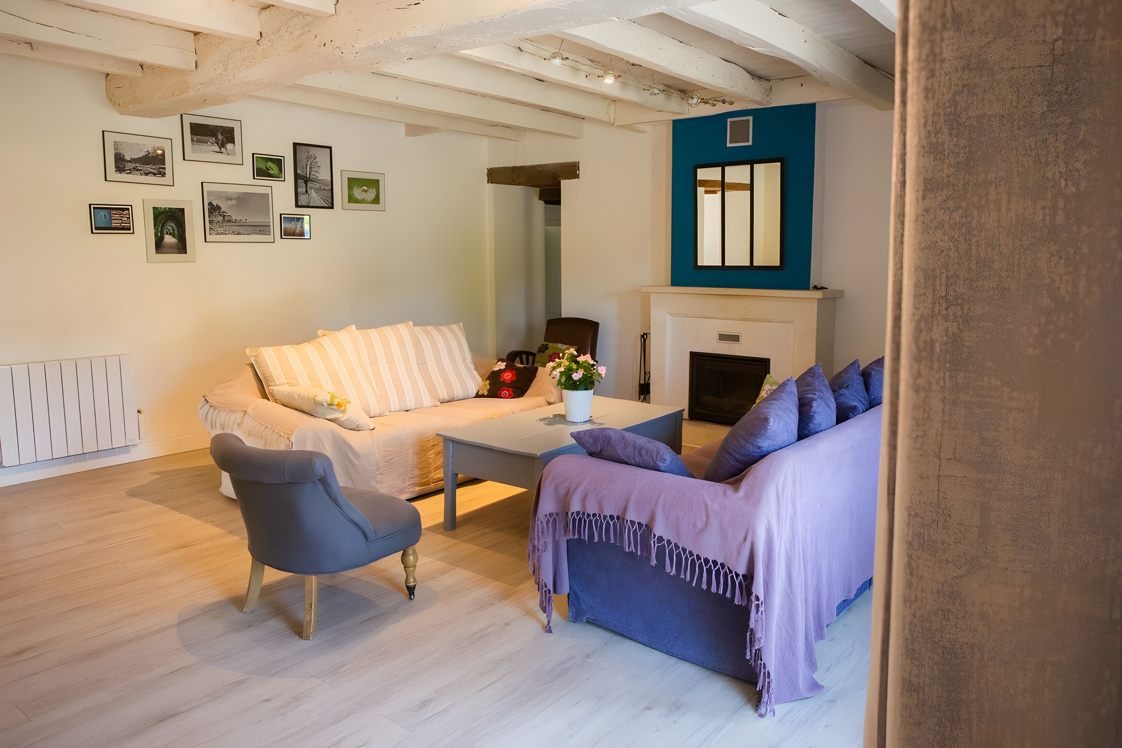 Un salon comprenant un canapé, un fauteuil et une table basse. On y trouve également une cheminée et un mur orné de tableaux encadrés.