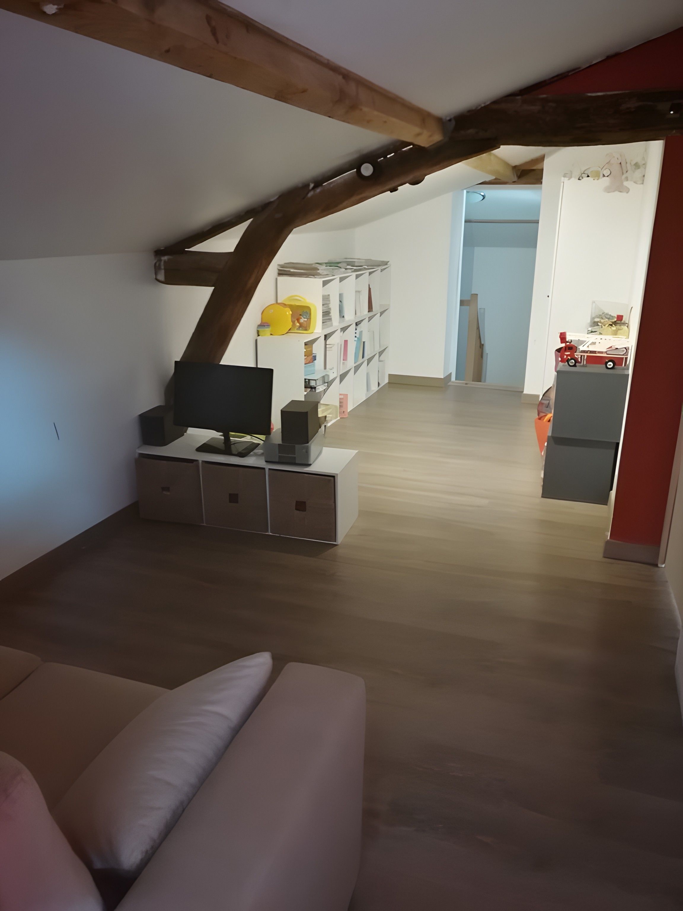 A room with a wooden ceiling, a television on a stand, a sofa, and a bookshelf filled with books and toys.