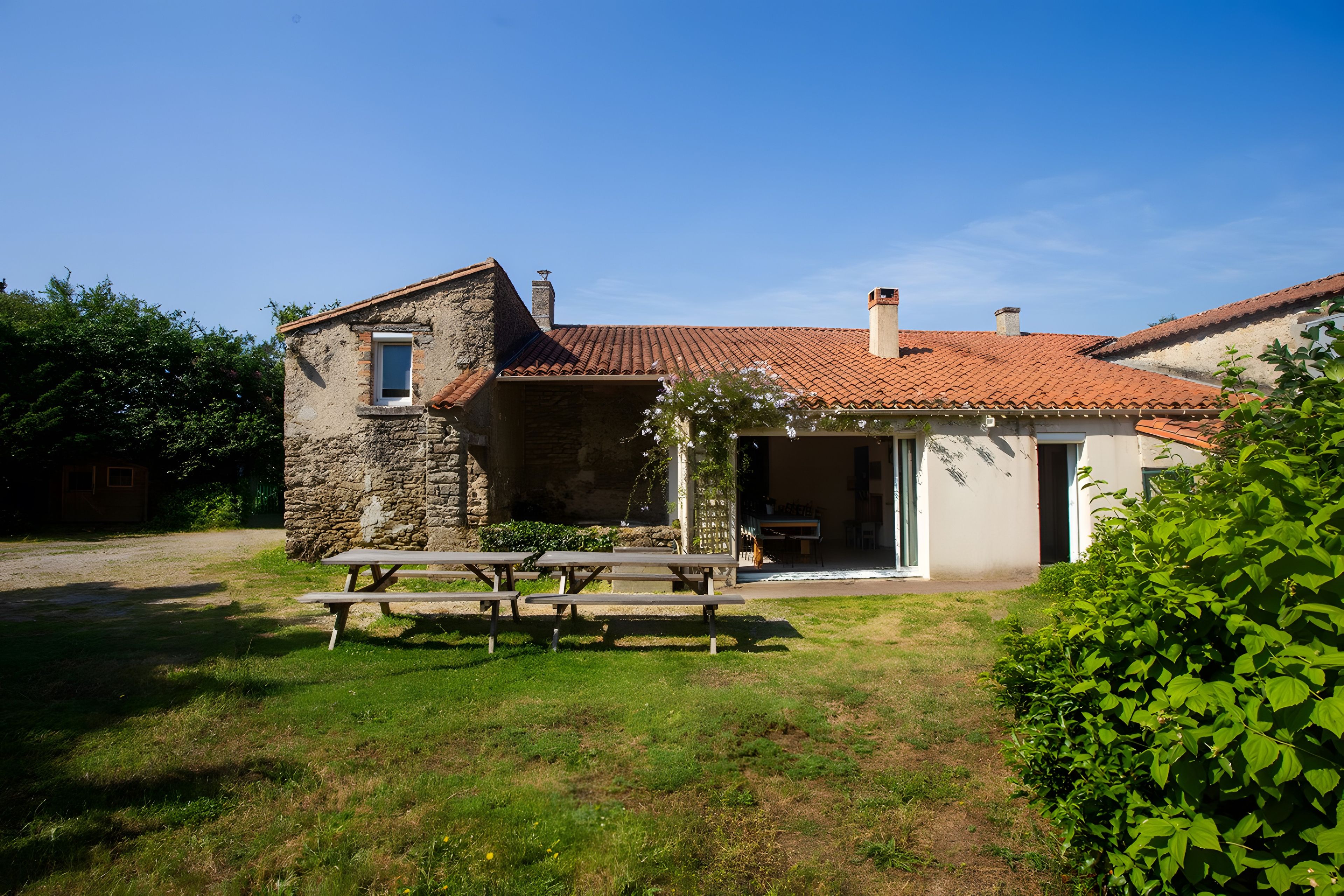 Un bâtiment rustique en pierre, avec un toit en tuiles, un banc en bois et un espace jardin.