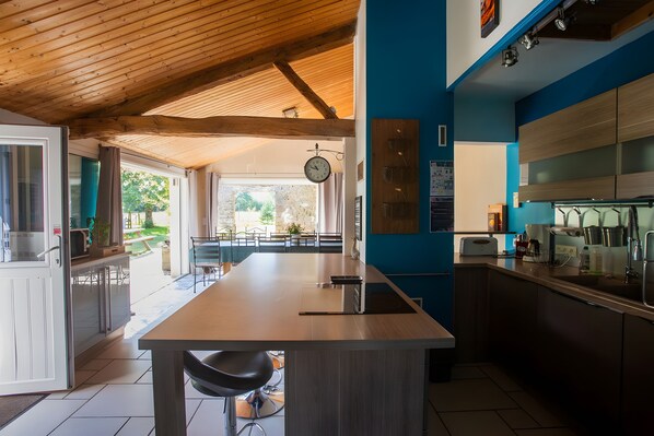 A modern kitchen with a wooden ceiling, a central island with a sink, and a dining area with a view of the garden.