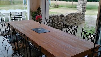Een eetruimte met een houten tafel en stoelen, een bloevas en uitzicht op de tuin via glazen deuren.