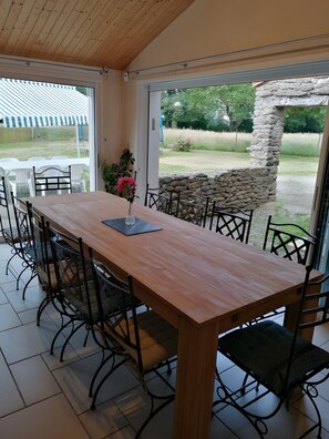 Een eetruimte met een houten tafel en stoelen, een bloevas en uitzicht op de tuin via glazen deuren.