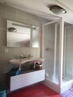 Een badkamer met een wit wastafelmeubel, spiegel en douchecabine.