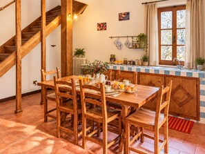 A wooden dining table with chairs, a kitchen area with a window, and a staircase.