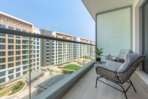 A balcony with a view of a modern building complex, a seating area with a chair and a small table, and a potted plant. - Contemporary 1BR with Partial Sea View, Private Beach Access (Khor Fakkan)