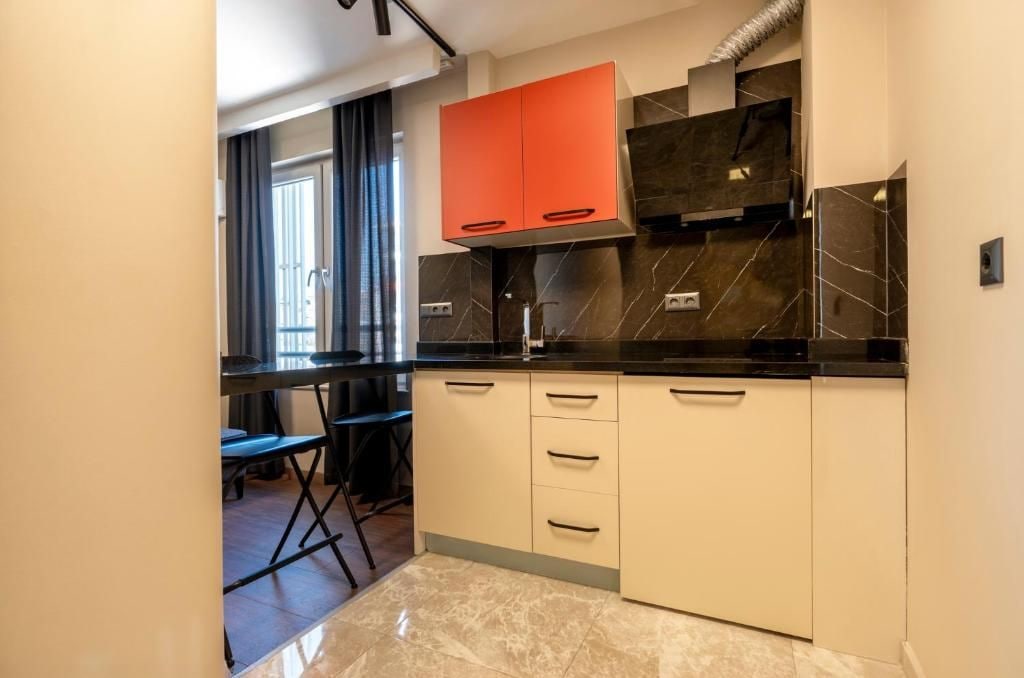 A modern kitchen with a black countertop, white cabinets, and a red upper cabinet.