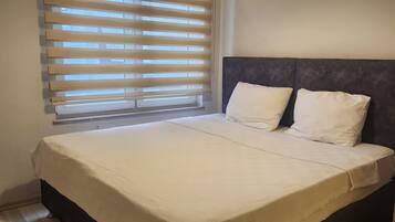 A bedroom with a bed, a window with blinds, a ceiling light, and a wall-mounted air conditioning unit.