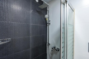 A shower area with a black tiled wall, a glass shower door, and a handheld showerhead. - Premium Rezidans Otel (Muratpasa)