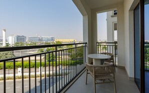A balcony with a table and chairs, a view of a cityscape including a building with a distinctive logo, and a clear sky. - Serene Yas Island Hideaway w/ Resort Facilities (Abu Dhabi)