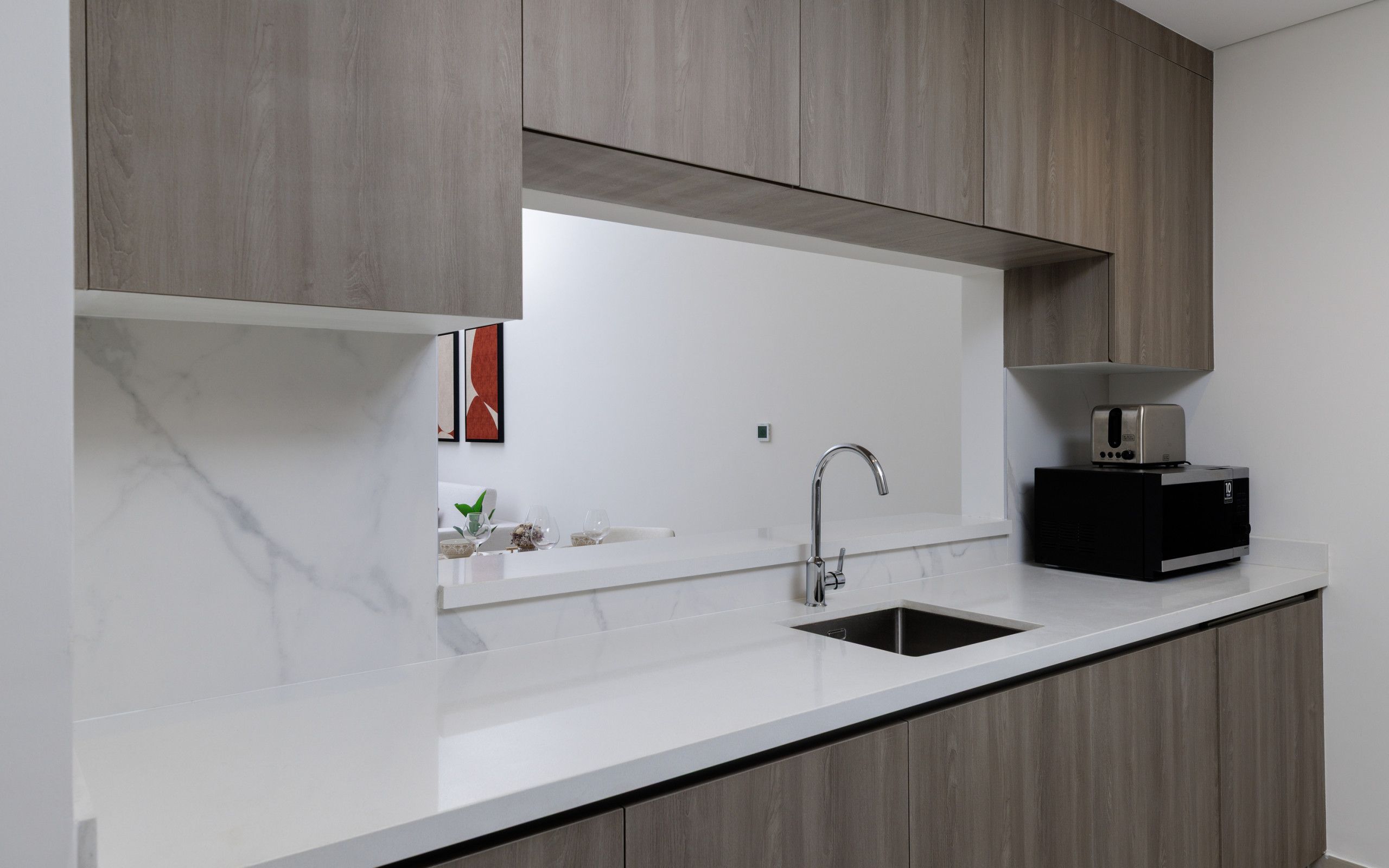 A modern kitchen with a white countertop, a stainless steel sink, and a black coffee machine.
