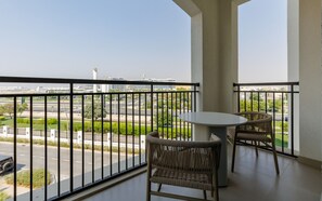 A balcony with a table and two wicker chairs, overlooking a road and buildings. - Serene Yas Island Hideaway w/ Resort Facilities (Abu Dhabi)