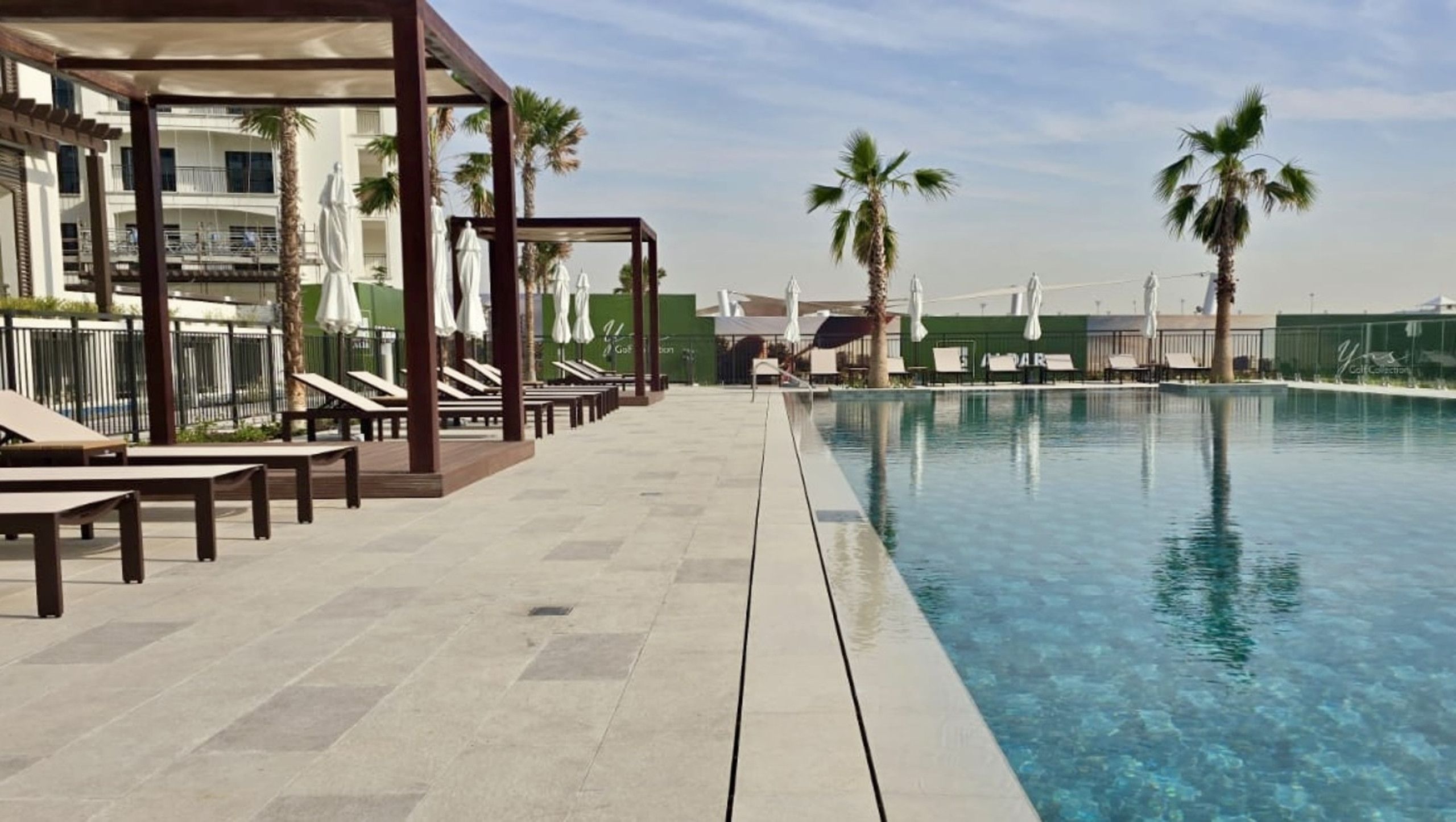 A pool area with lounge chairs and umbrellas, a clear pool, and palm trees.