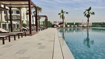 A pool area with lounge chairs and umbrellas, a clear pool, and palm trees.