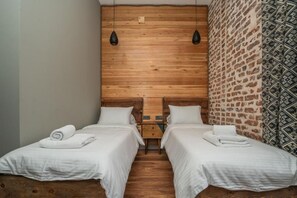 A room with two beds, wooden headboards, and a brick-patterned wall.