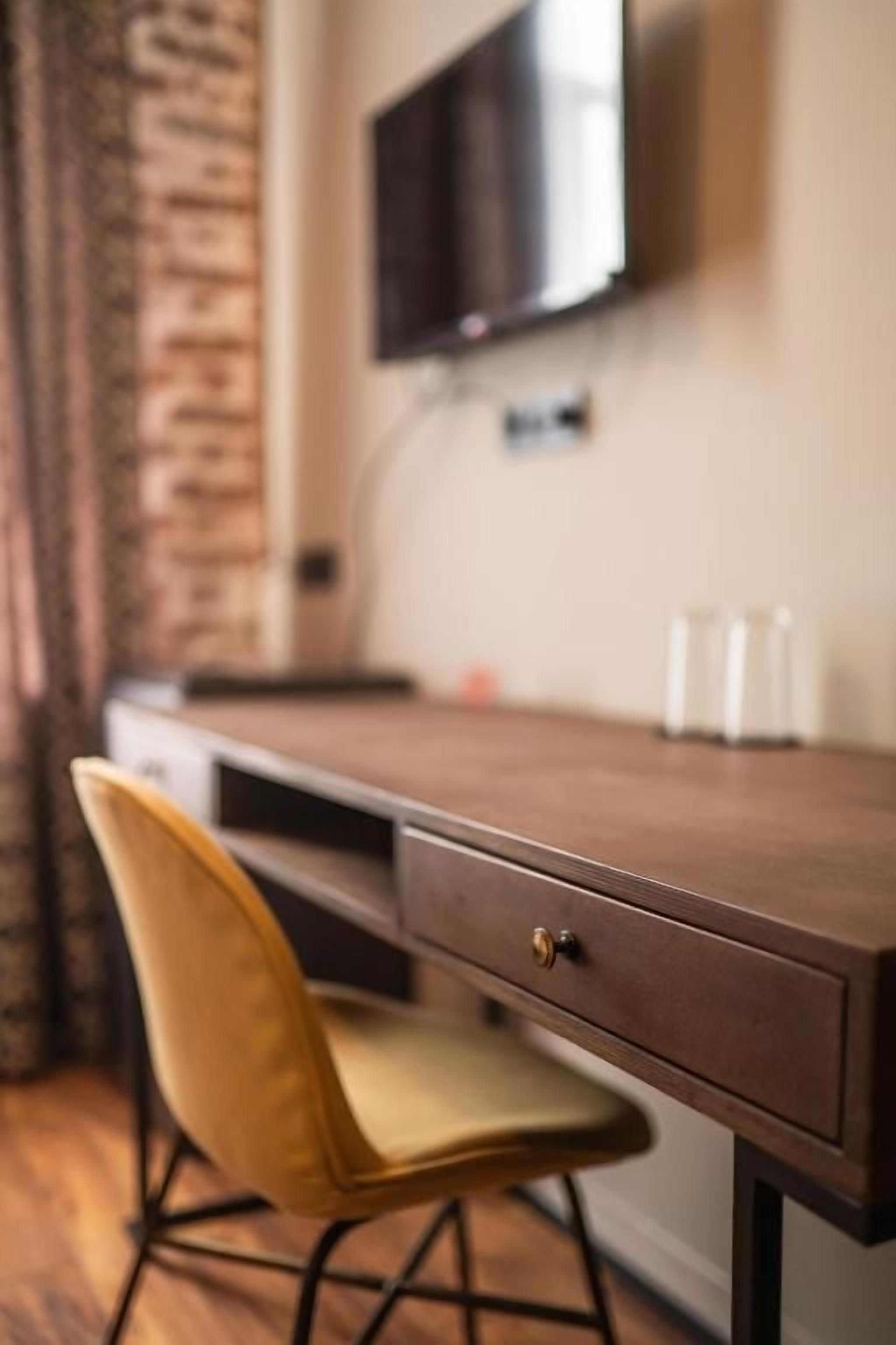 A wooden desk with a drawer, a yellow chair, and a television mounted on the wall.