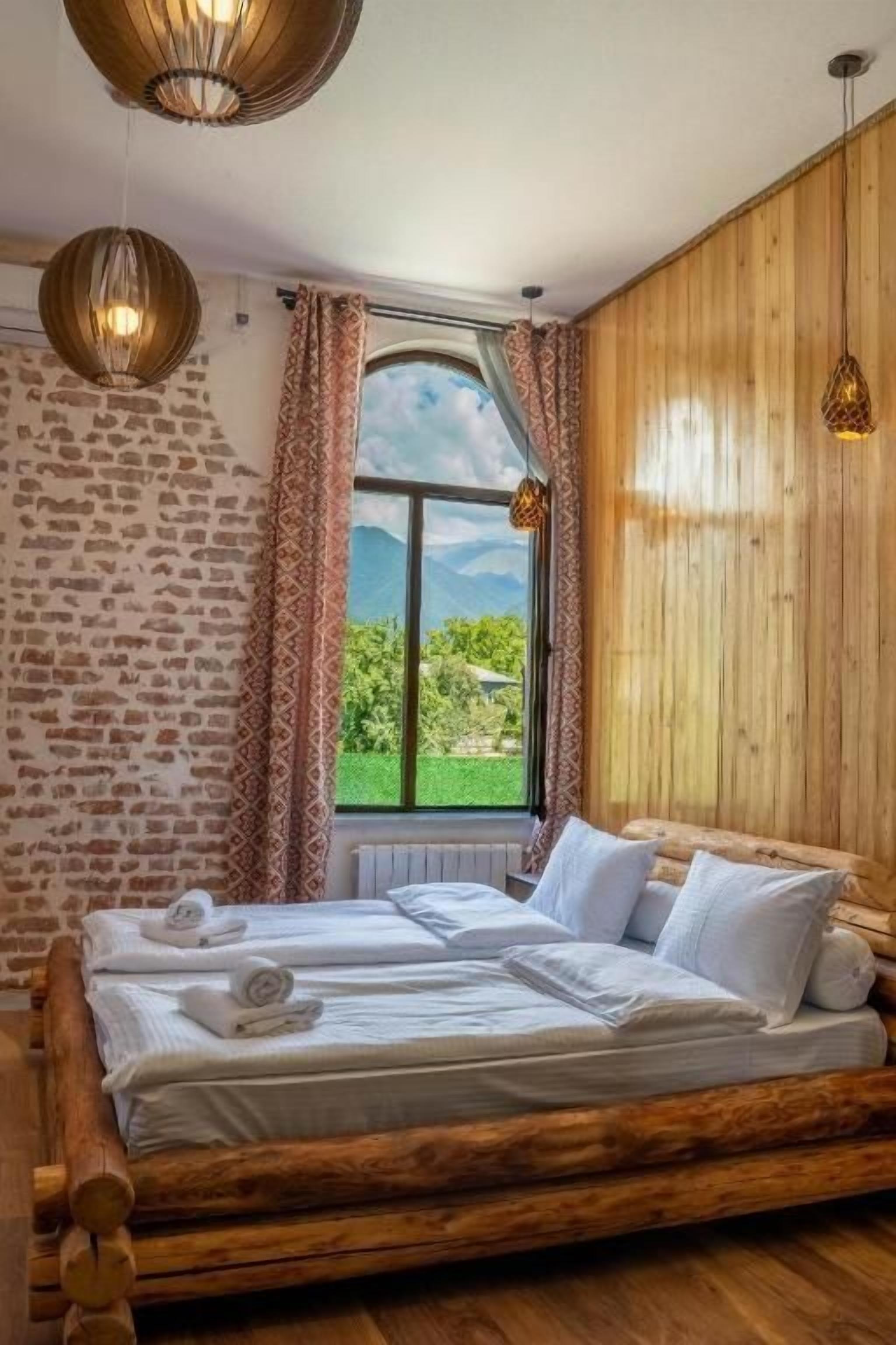 Une pièce avec un lit, des murs en bois, une fenêtre avec des rideaux et des lampes suspendues.