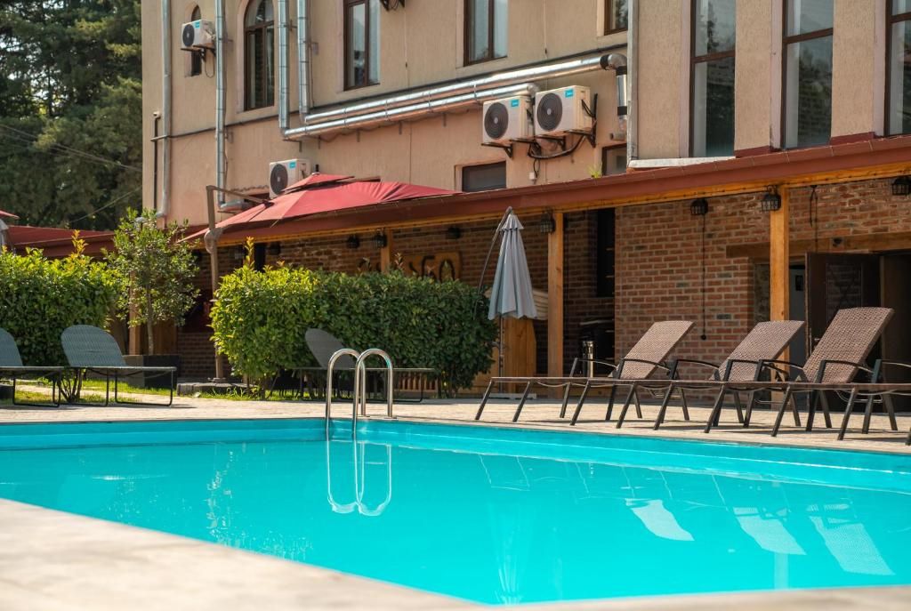 Une piscine avec des chaises longues et des parasols, un bâtiment en briques doté de climatiseurs et un auvent rouge.