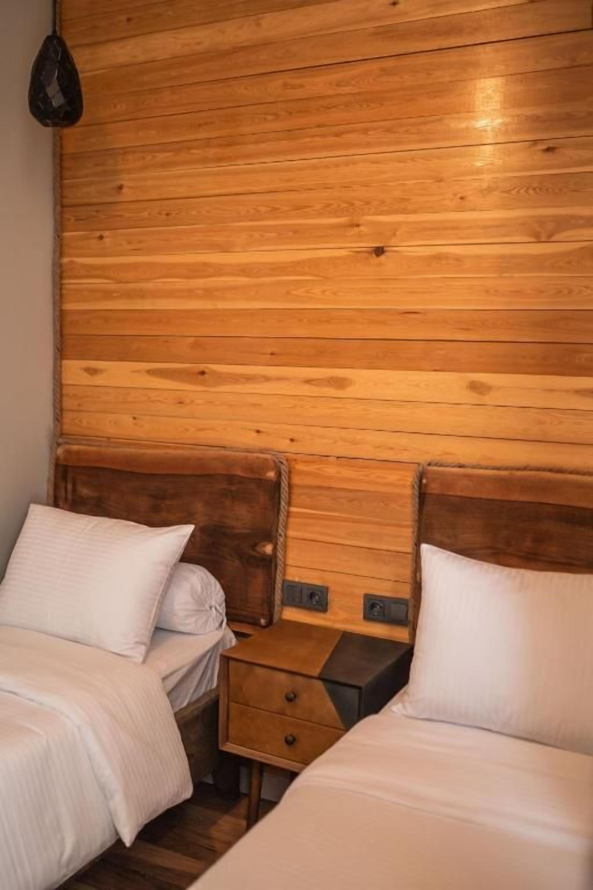 A room with two beds, wooden headboard, and a nightstand with drawers.