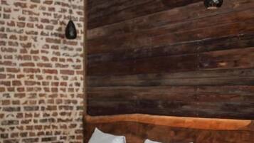 Un lit avec du linge de lit blanc, une tête de lit en bois et un mur en briques.