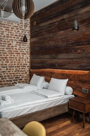 A bed with white linens, a wooden headboard, and a brick wall.