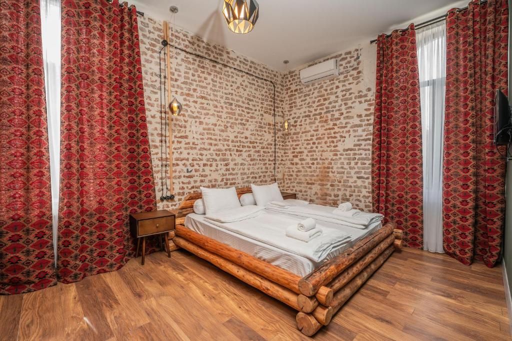 Una habitación con pared de ladrillo, estructura de cama de madera y cortinas rojas con estampado.