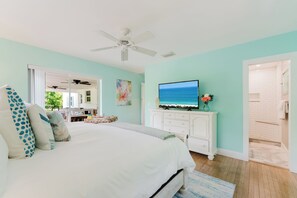A bedroom with a bed, a television on a dresser, and a view of the ocean through the window. - Juno Breeze | Hot Tub | Walk to Beach | Sleeps 9! (Juno Beach)