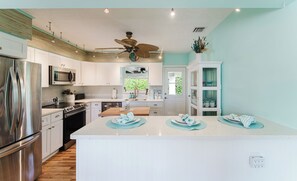 A modern kitchen with stainless steel appliances, a central island, and a ceiling fan. - Juno Breeze | Hot Tub | Walk to Beach | Sleeps 9! (Juno Beach)