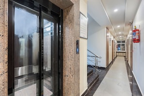 A hotel corridor with a fire extinguisher, emergency exit sign, and a staircase. - Treebo Skanda Grande (Puducherry)
