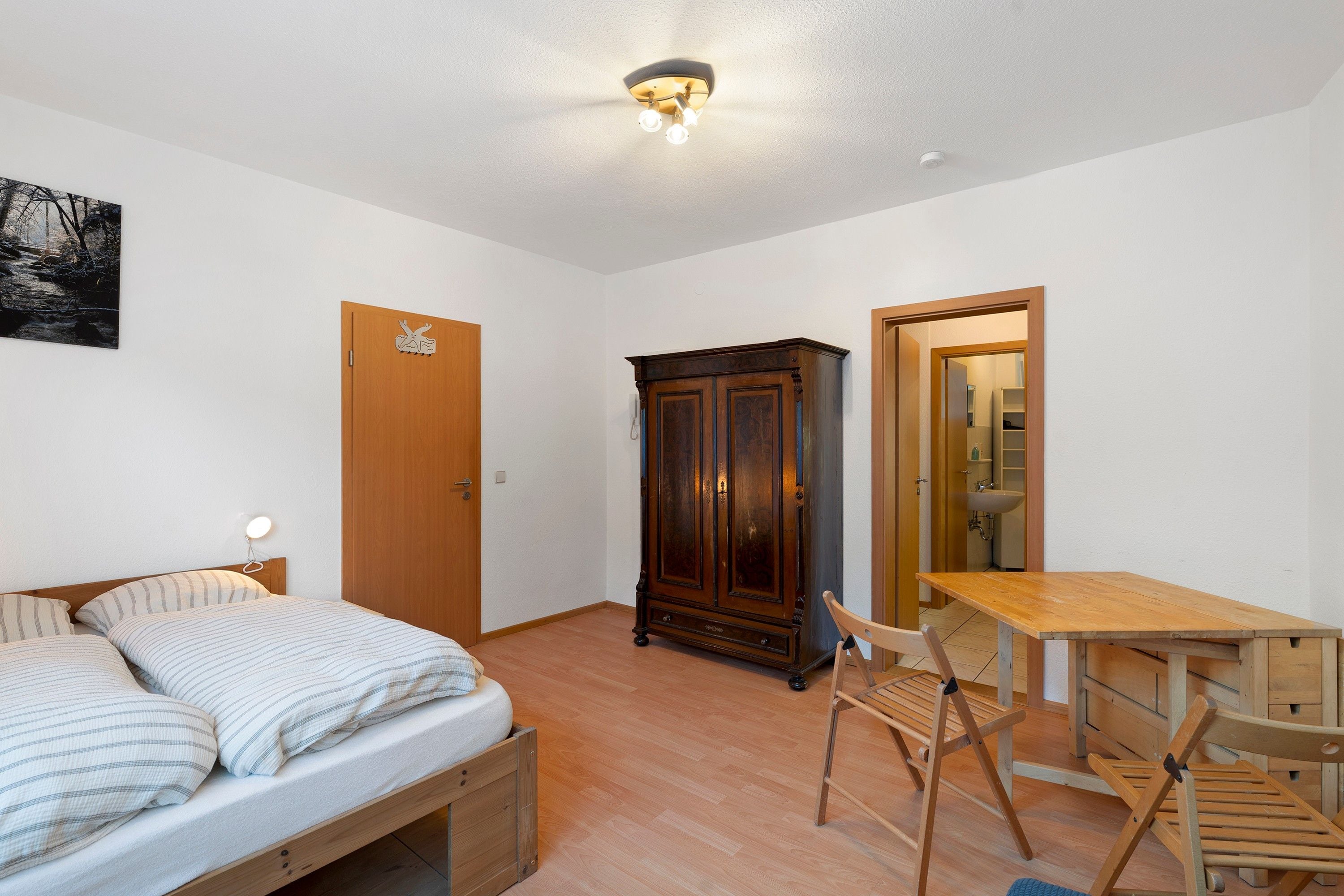 Un dormitorio con una cama, un armario de madera, una mesa y una silla.