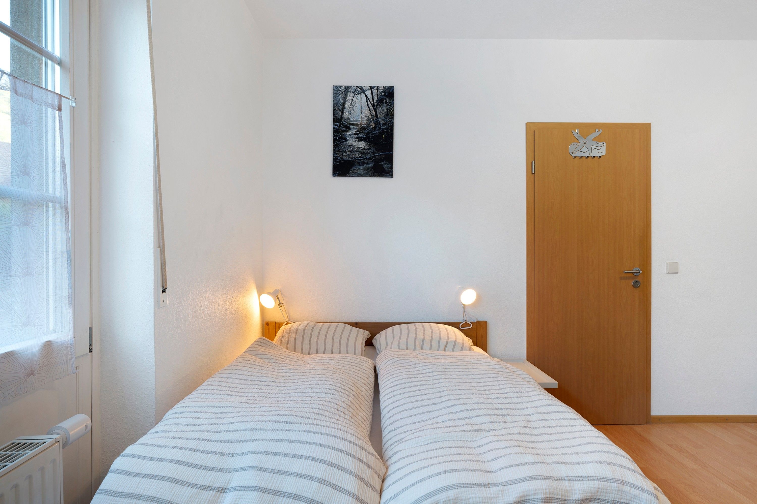 A bedroom with a bed, bedside lamps, a door, and a window.