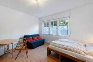 A room with a wooden floor, a blue sofa with red cushions, a wooden bed, a small wooden table, and a window with curtains. - Apartment 'Mittendrin' with Wi-Fi (Bühlertal)