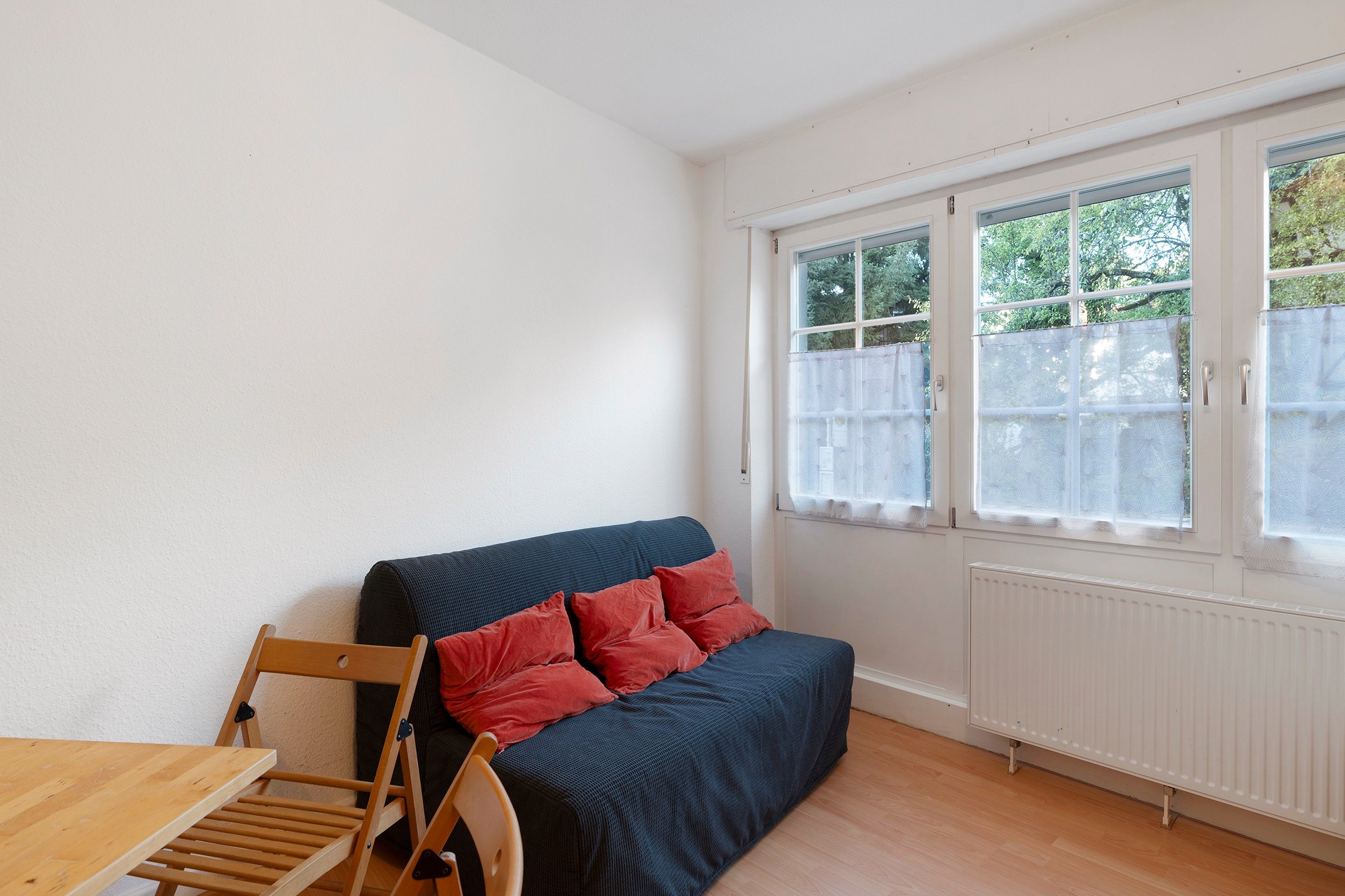 Una habitación pequeña y poco amueblada con un sofá, una silla de madera y una mesa.