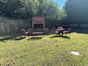 A backyard with a brick fire pit, wicker furniture, and a wooden fence. - Shipwrecked  - In Town 3 BR House, Cottage, Play Barn, brick fire pit & Pool. (Chincoteague)