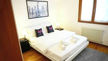Una camera d'albergo con un letto, cuscini, un comodino, una lampada, un quadro appeso al muro e una finestra.