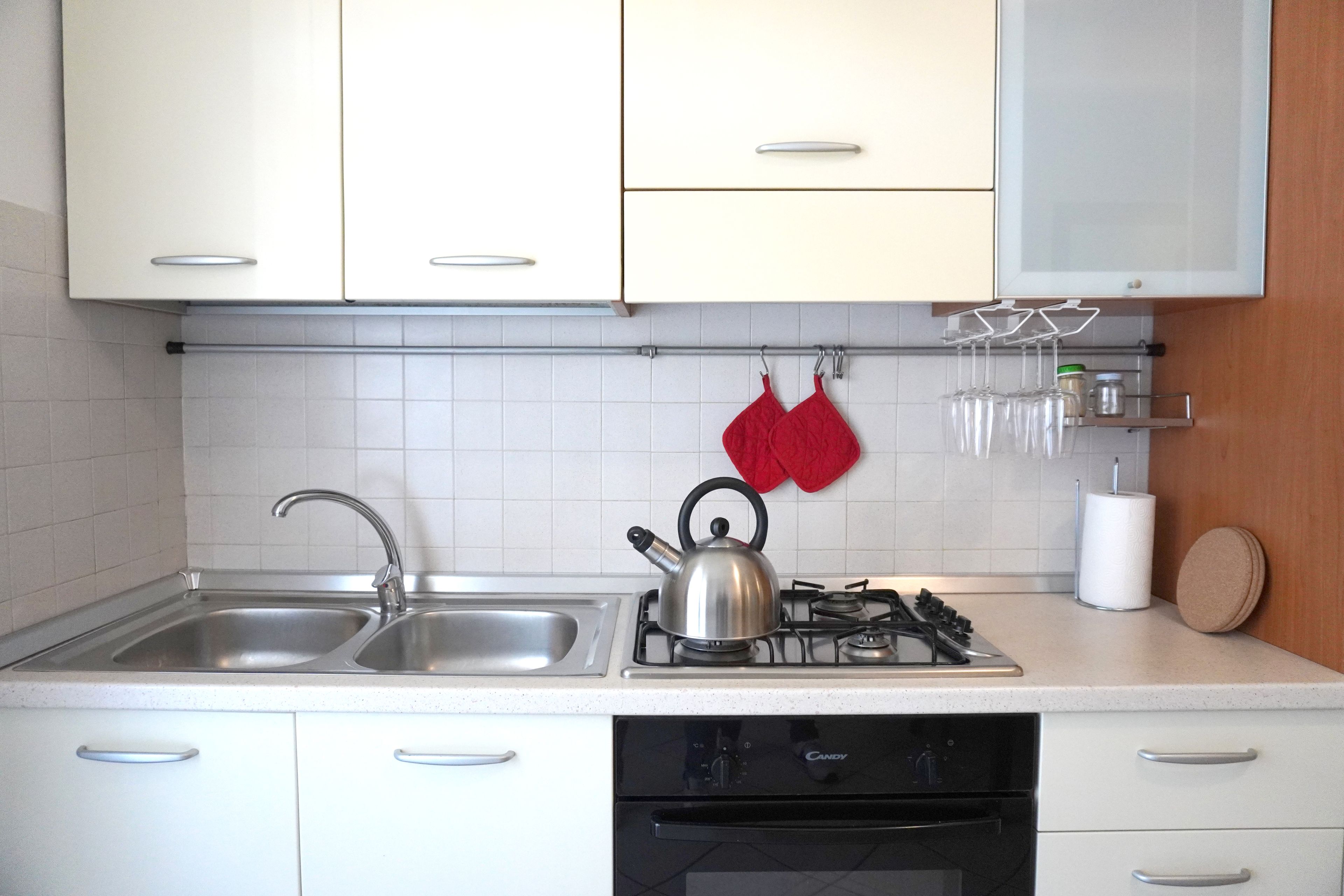 A kitchen with a double sink, a kettle, a stove, and a dishwasher.