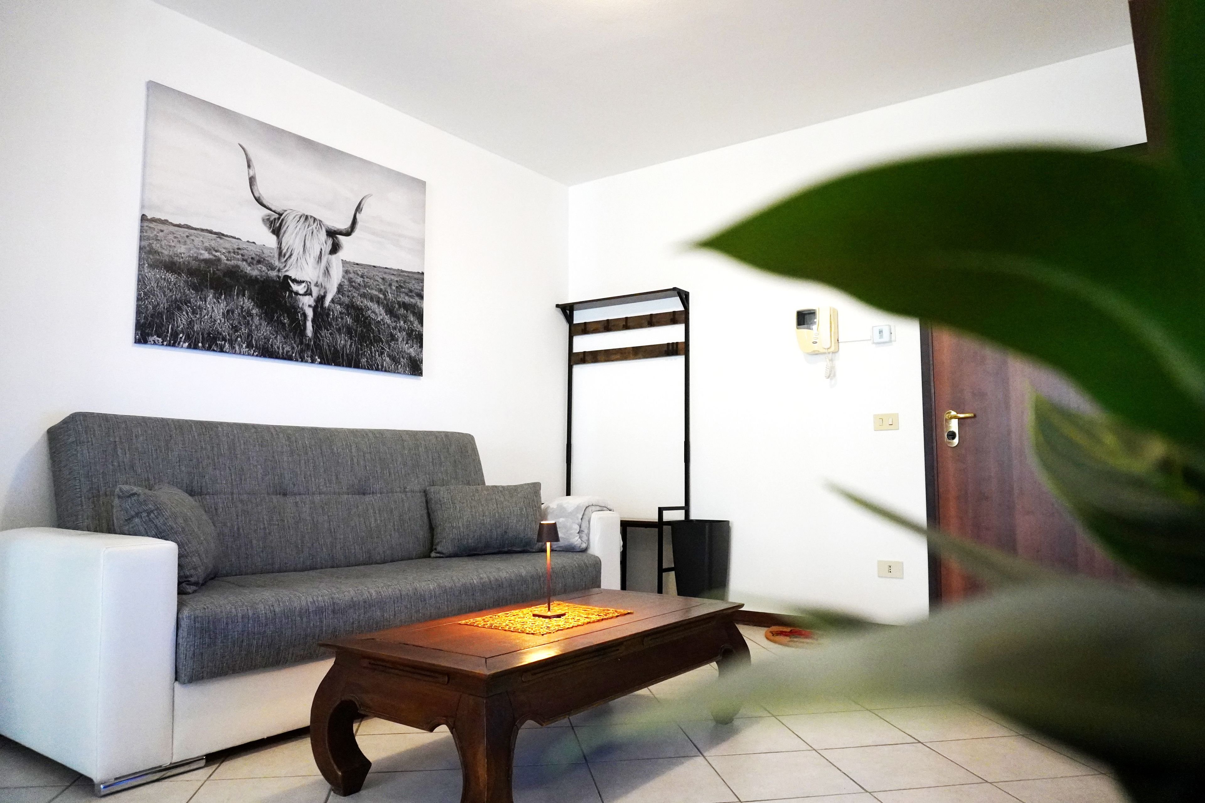 A living room with a grey sofa, a wooden coffee table, a black floor lamp, and a wall-mounted light fixture.