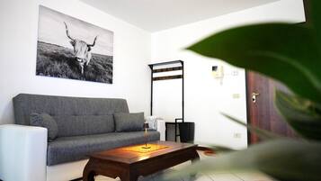 A living room with a grey sofa, a wooden coffee table, a black floor lamp, and a wall-mounted light fixture.