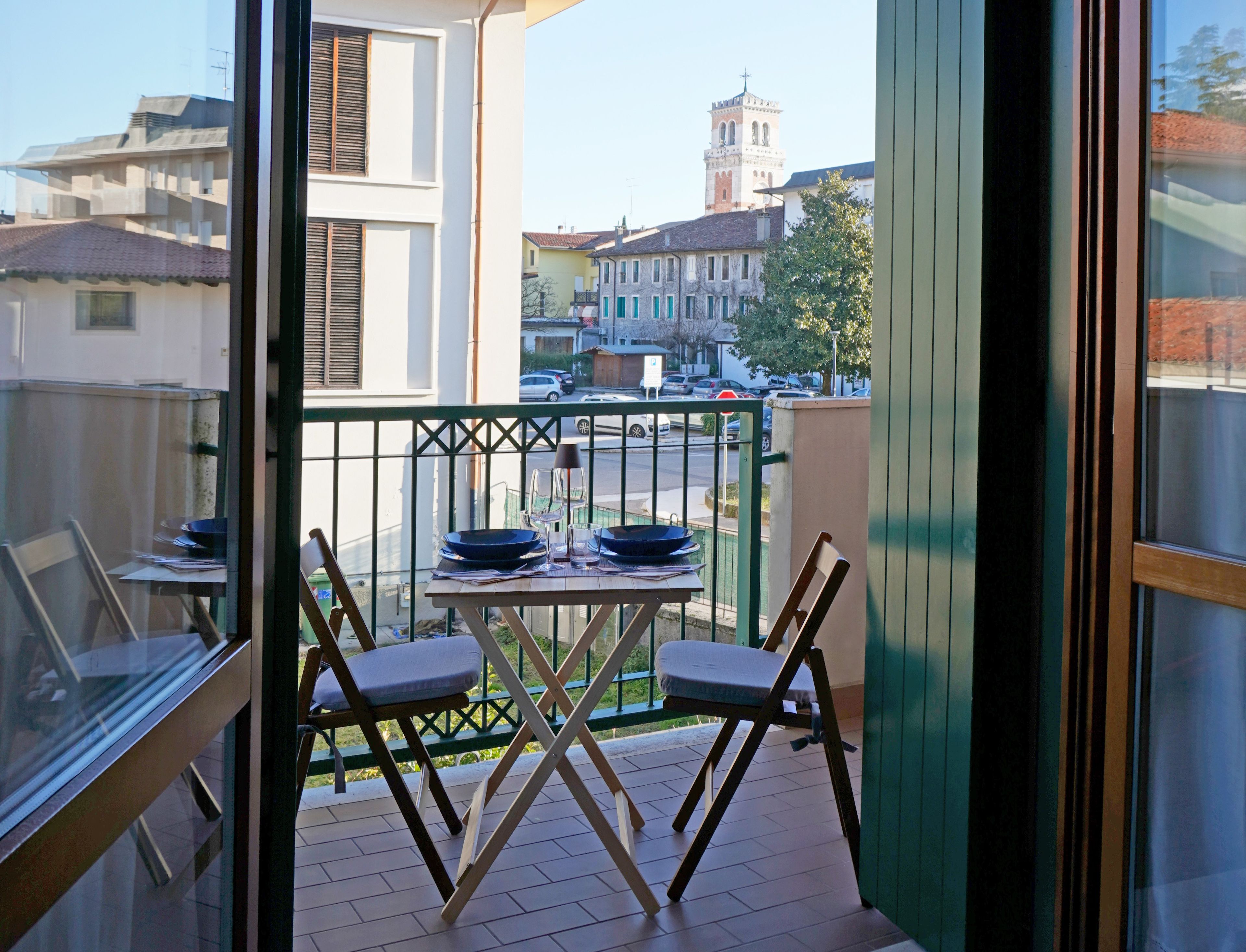 Een balkon met een eettafel, een stoel en uitzicht op een straat met gebouwen en een toren.