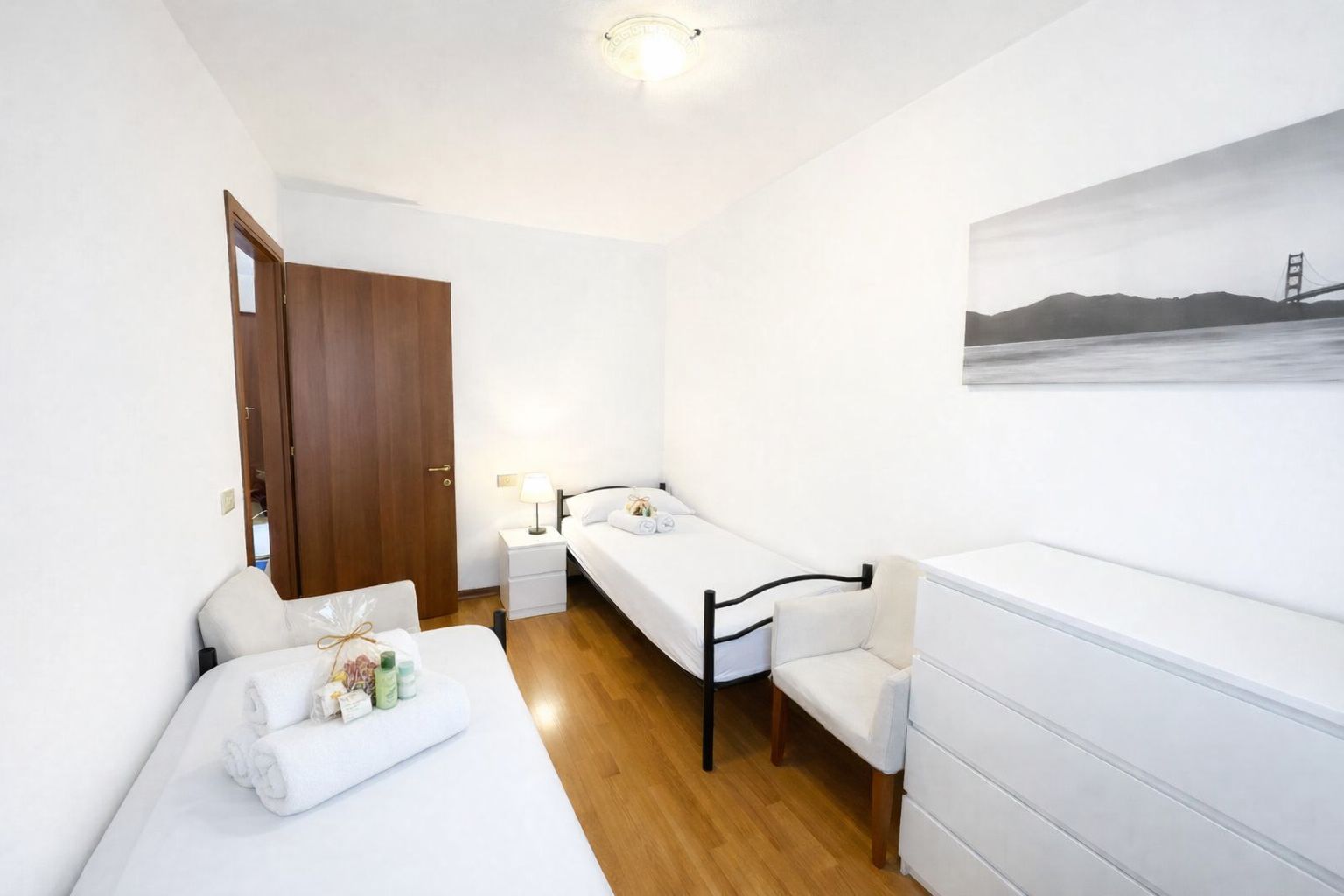 A hotel room with a bed, bedside table, chair, and a painting on the wall.