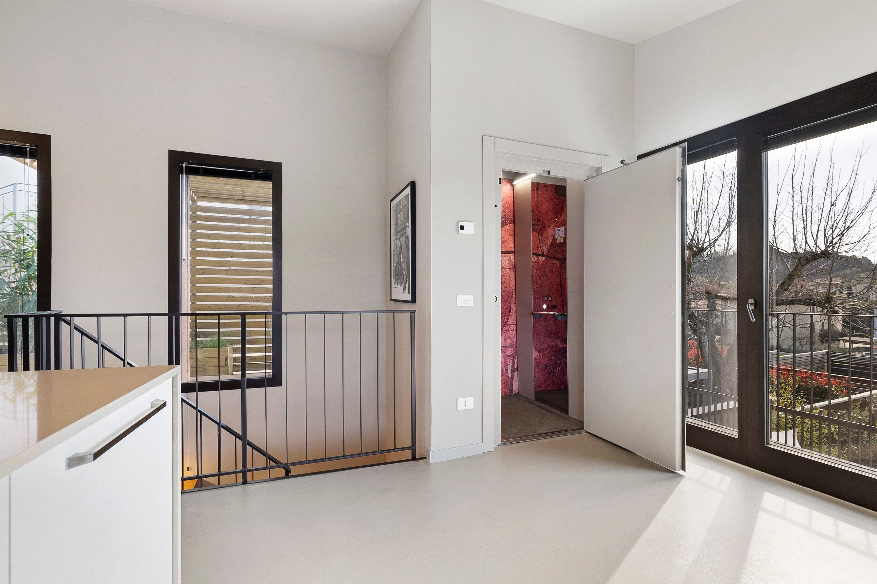 Ein modernes Interieur mit einer Treppe, einer Tür zu einem roten Raum und einem großen Fenster mit Blick.